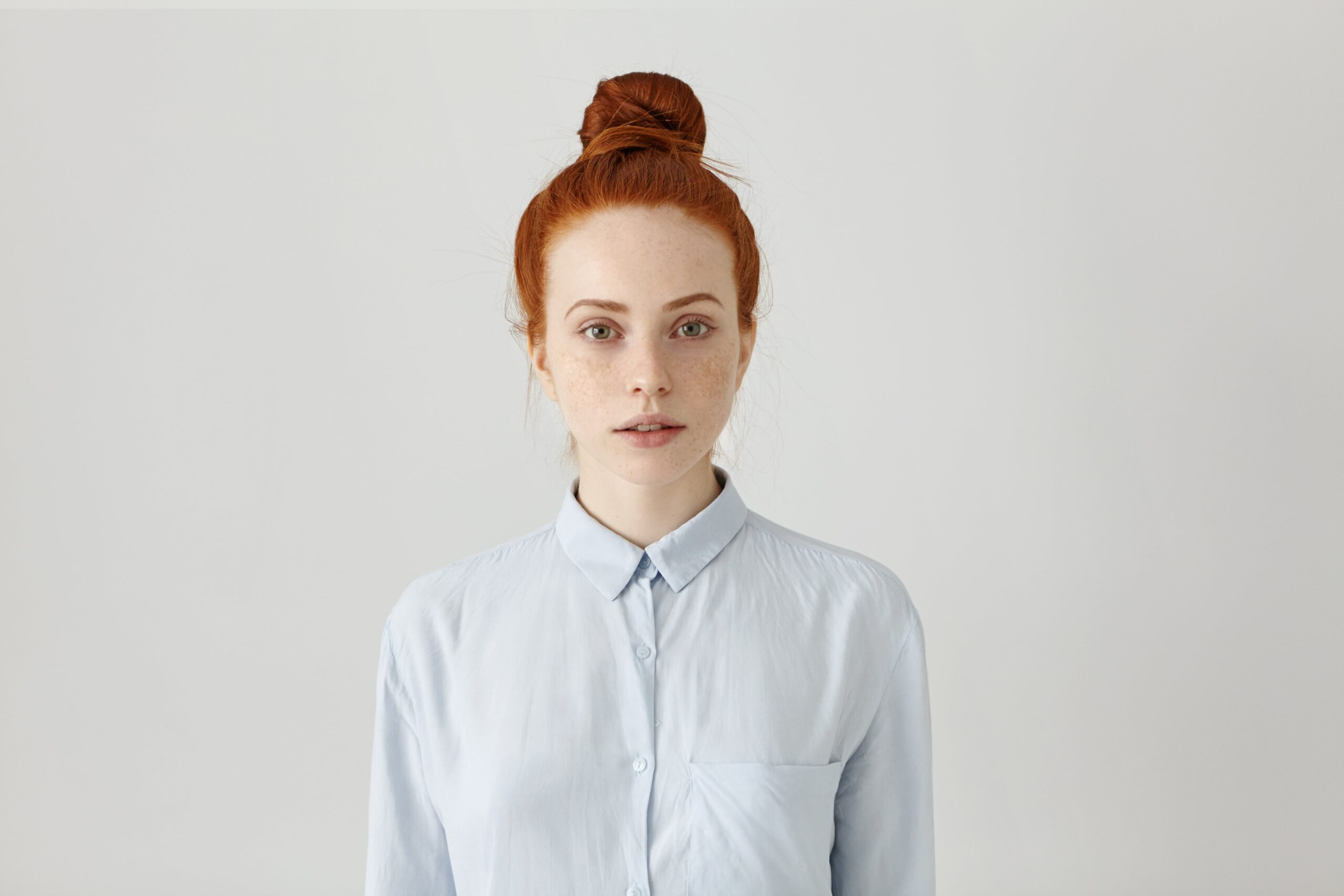 beautiful-young-redhead-female-employee-with-hair-bun-posing-indoors-dressed-light-blue-formal-shirt-getting-prepared-work-having-serious-look-horizontal-isolated-shot-min beautiful-young-redhead-female-employee-with-hair-bun-posing-indoors-dressed-light-blue-formal-shirt-getting-prepared-work-having-serious-look-horizontal-isolated-shot-min
