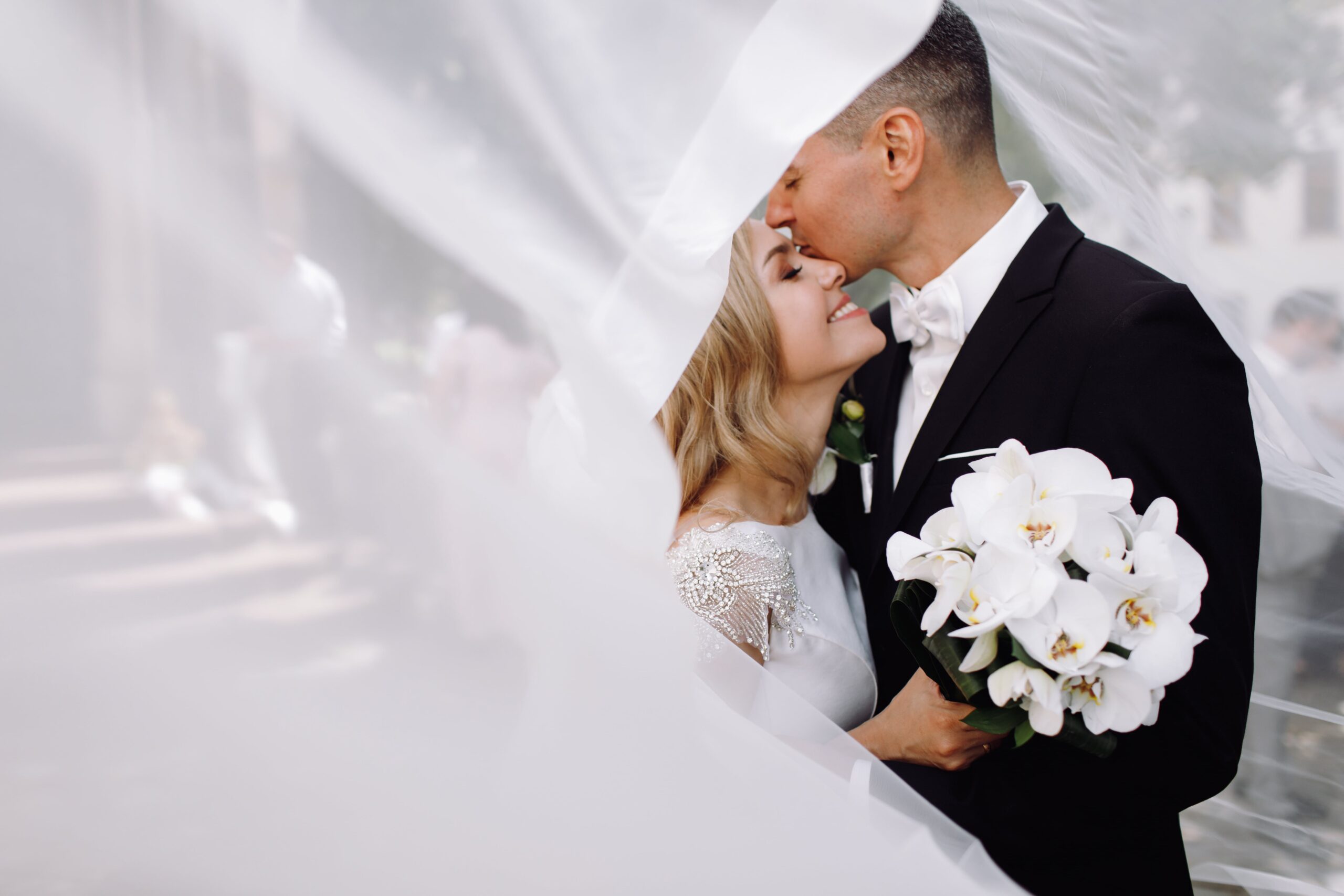 groom-black-tuxedo-hugs-tender-stunning-bride-while-they-stand-min groom-black-tuxedo-hugs-tender-stunning-bride-while-they-stand-min