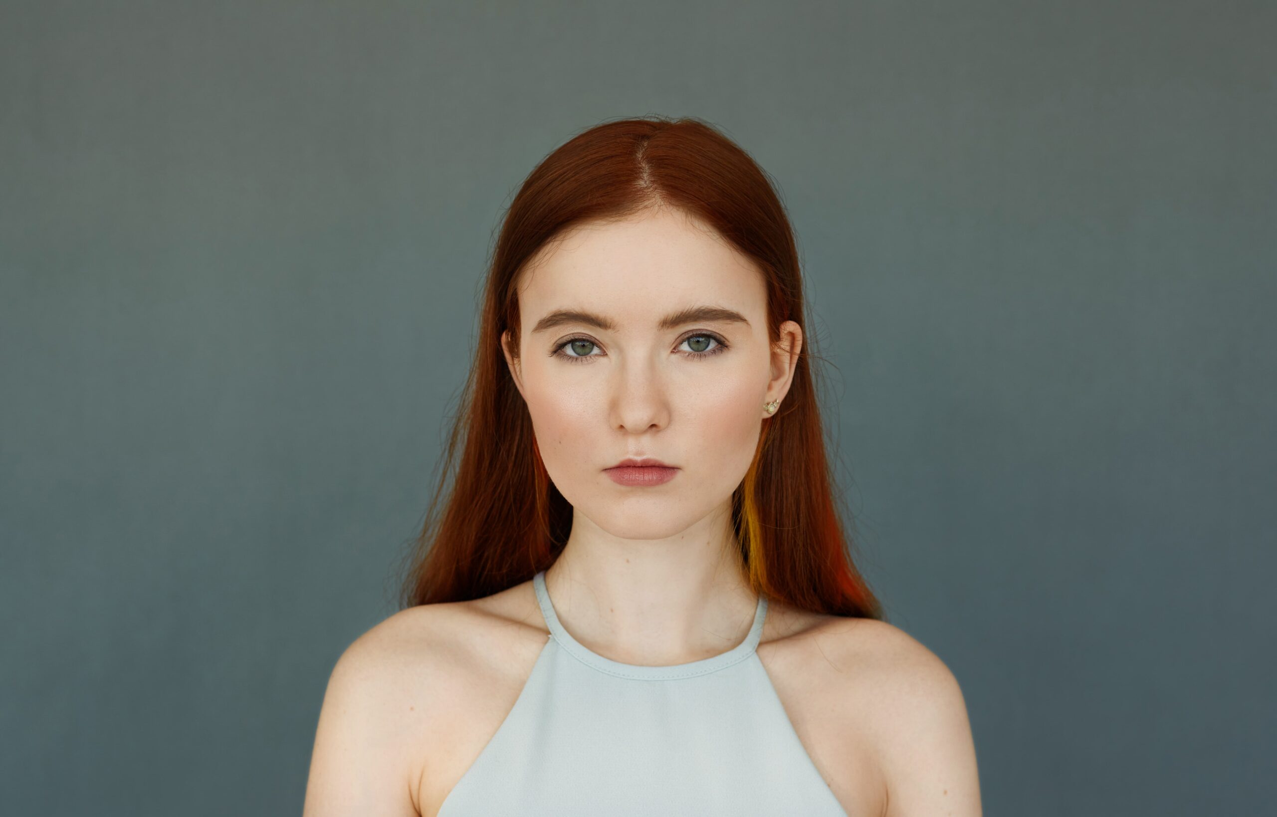 portrait-young-tender-redhead-teenage-girl-with-green-eyes-wearing-blue-top-looking-with-serious-pensive-expression-standing-blue-wall-her-lips-slightly-parted-min