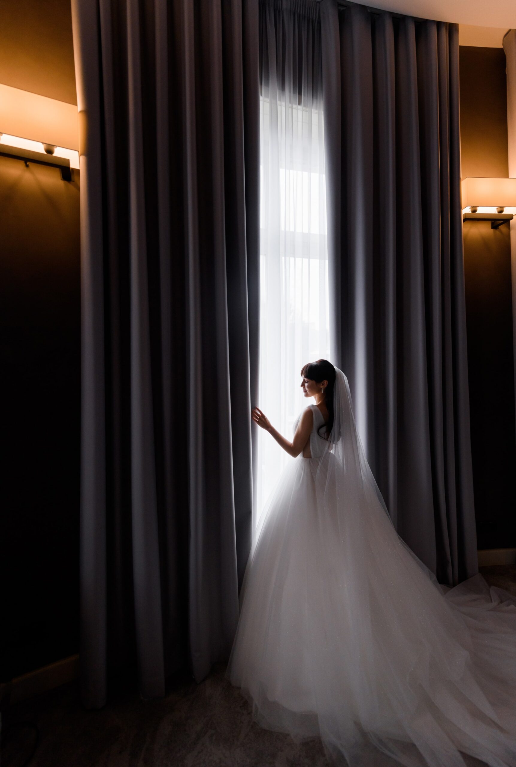 side-view-beautiful-brunette-bride-standing-by-window-morning-dark-hotel-room-min side-view-beautiful-brunette-bride-standing-by-window-morning-dark-hotel-room-min